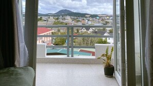 Un balcón con una planta en maceta, vista a un pueblo y cielo nublado.