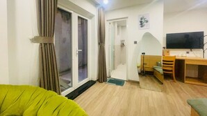 Una sala de estar con sofá, escritorio de madera, televisor y puerta corrediza de vidrio que da a un balcón.