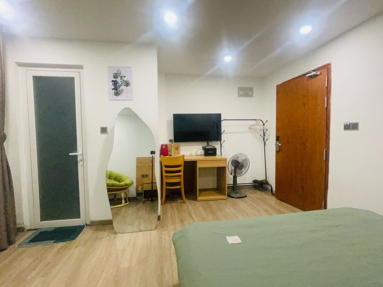 A compact room with a bed, a desk with a chair, a television, and a door.