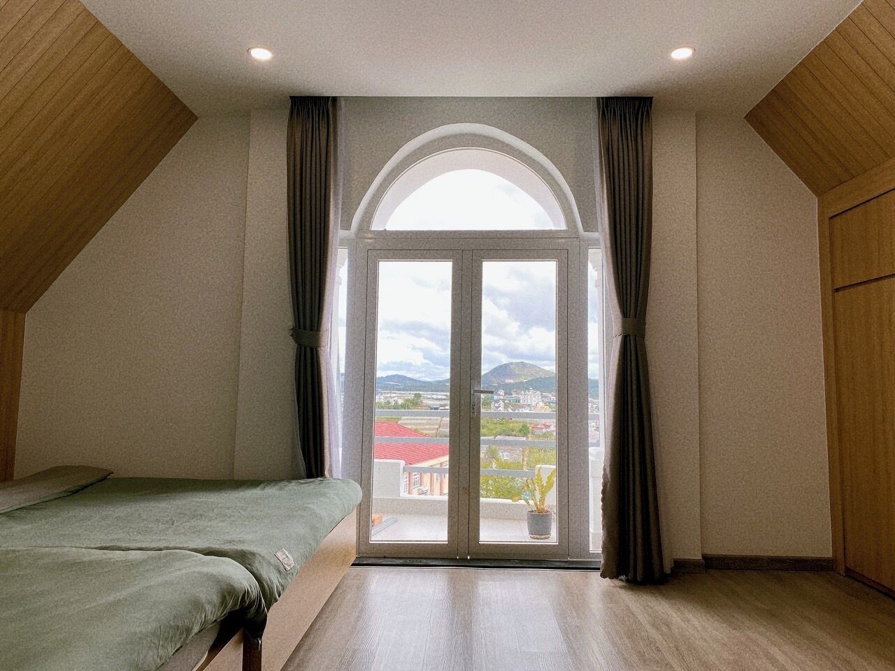 A bedroom with a bed, a large window with curtains, and a view of a cityscape.