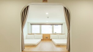 Una habitación con piso de madera, dos camas blancas con almohadas, una ventana y cortinas.