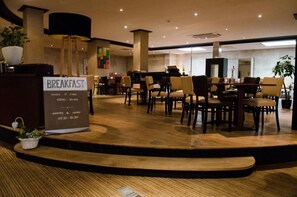 Enjoy breakfast in our spacious breakfast area, featuring multiple tables and a central pillar with decorative element.