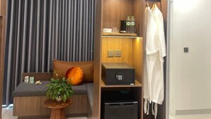 Une chambre d’hôtel moderne dotée d’un placard intégré, d’un coin salon avec un canapé et une petite table, ainsi que d’une plante en pot.