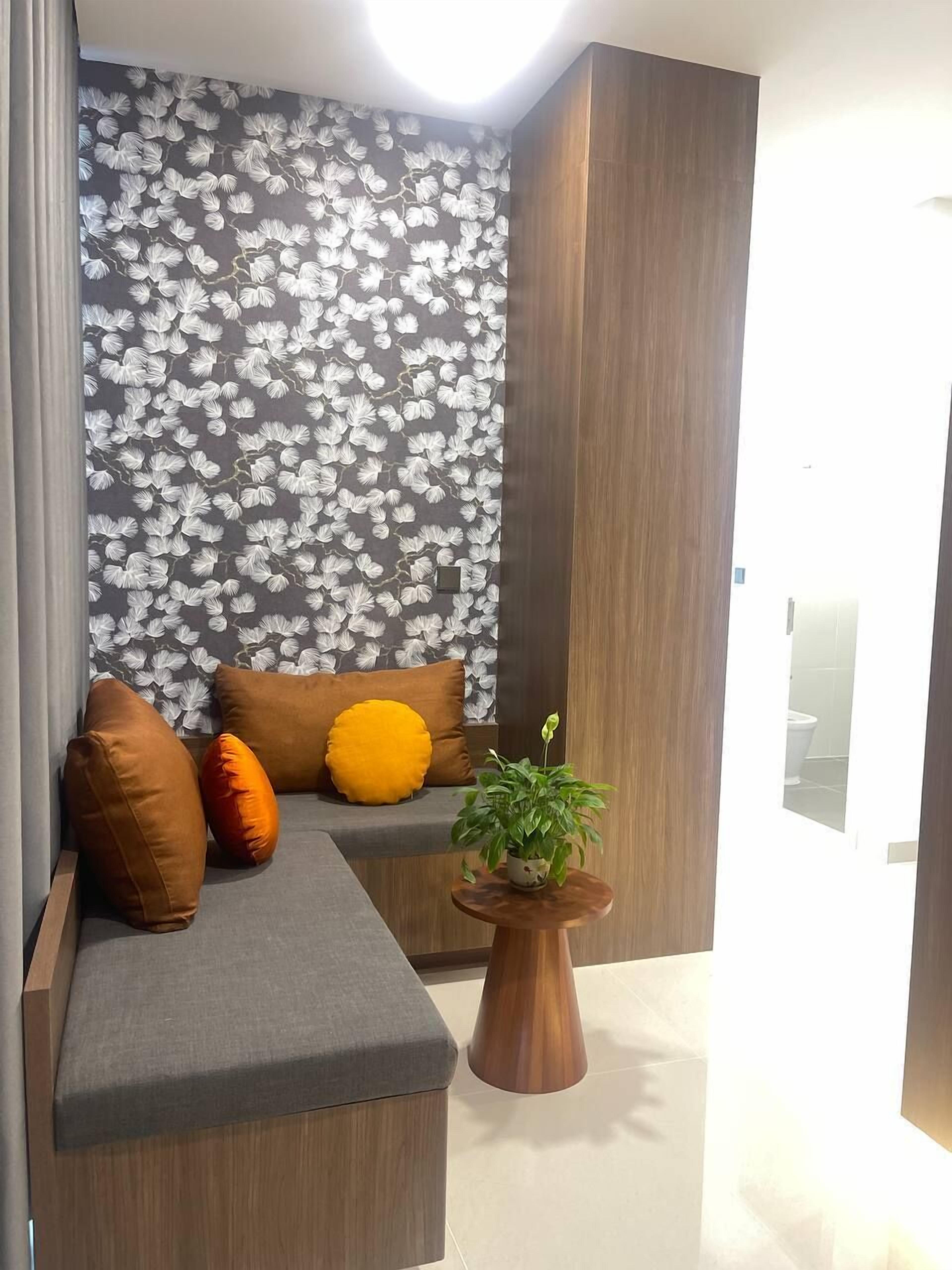 A modern living area with a grey sofa, brown and yellow cushions, a wooden side table with a plant, and a wall with a floral pattern.
