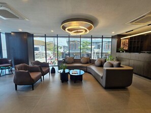 Een moderne lobby met een gebogen bank, twee fauteuils en een bijzettafeltje. Grote ramen bieden uitzicht op de stad.