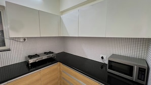 Cozinha com armários brancos, bancada preta, fogão e micro-ondas.