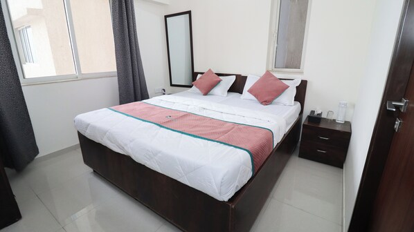 A neatly made bed with a white and pink quilt, a wooden headboard, and a nightstand with a glass and a tissue box.