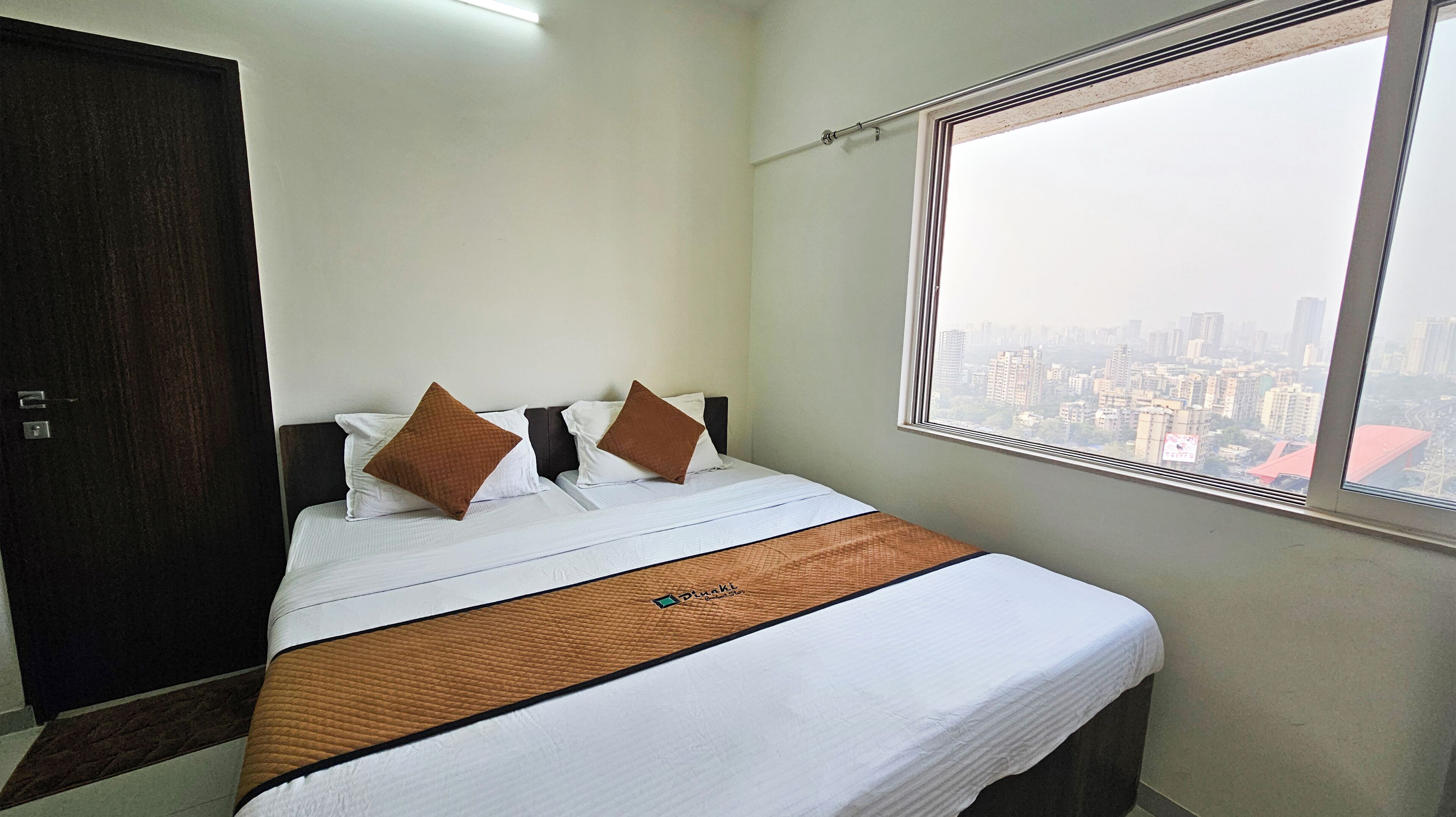 A hotel room with a bed, a window with a city view, and a dark wooden wardrobe.