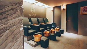 Zona de spa con sillones de masaje, cubos de madera y una pared con el logotipo 'RARA BEAUTY & MASSAGE'.