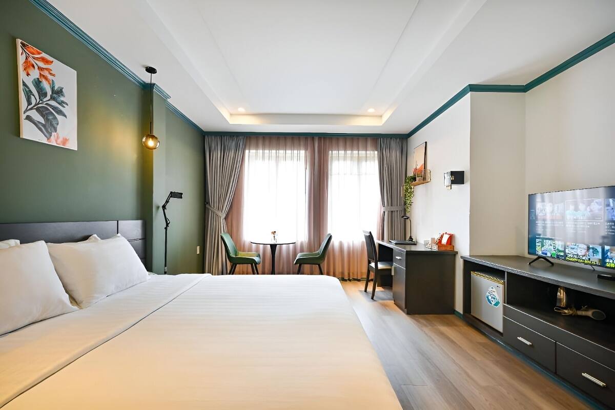 A hotel room with a bed, a desk, a chair, a television, and a painting on the wall.