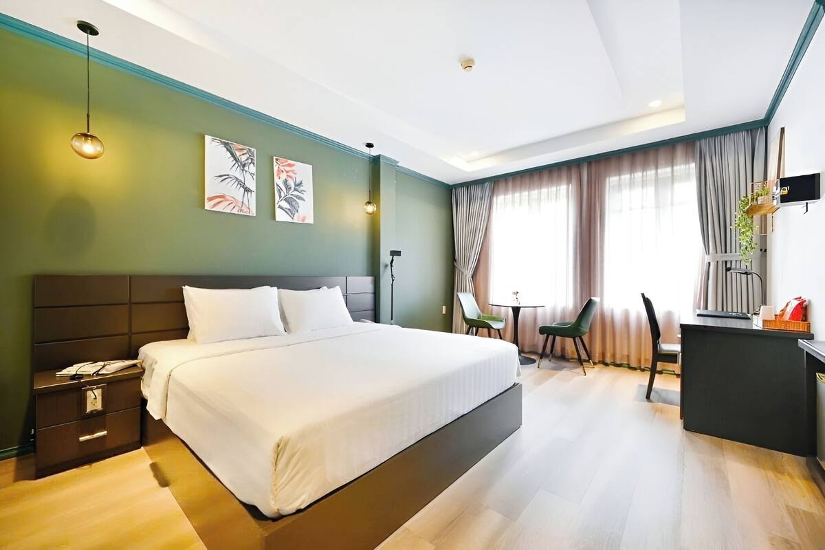 A modern hotel room with a large bed, a desk, a chair, a small table, and artwork on the walls.