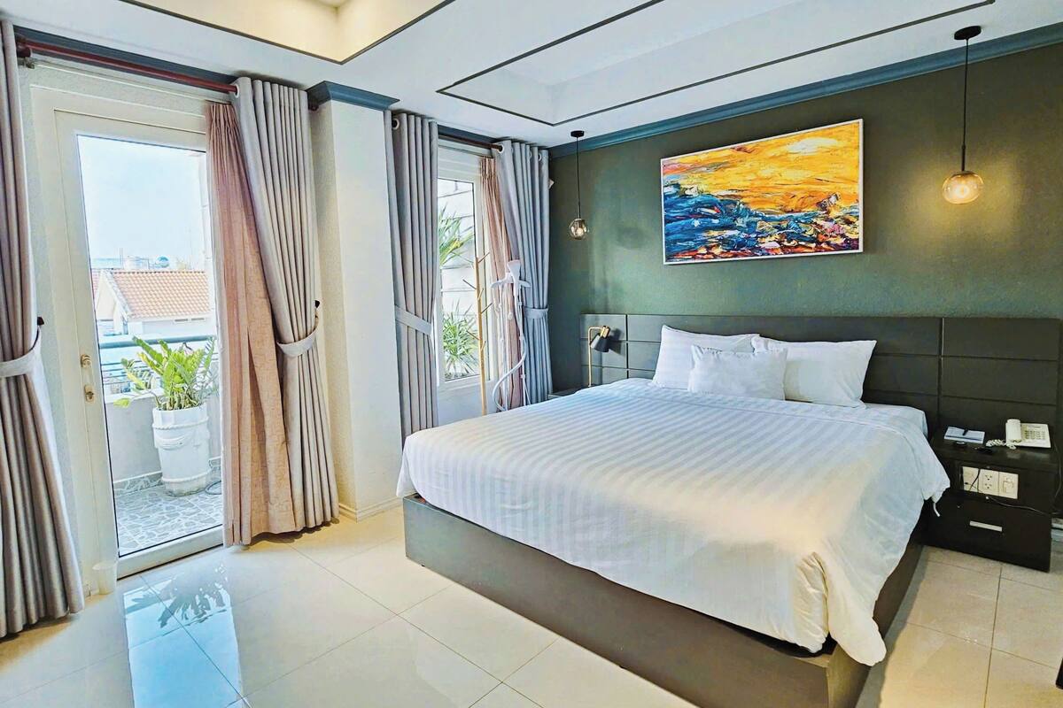 A modern hotel room with a large bed, a painting on the wall, and a balcony with curtains.