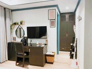 Una habitación de hotel compacta con escritorio, silla, televisor, armario y espejo.