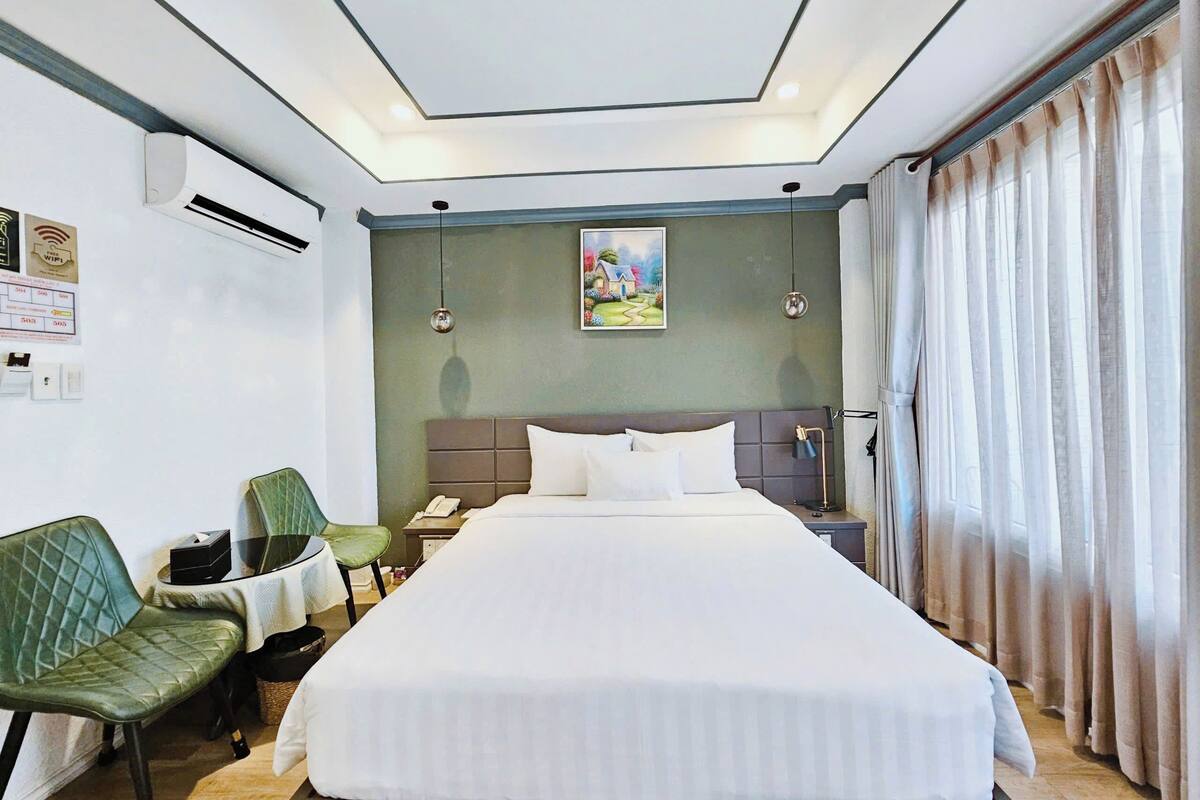 A hotel room with a bed, a desk, a chair, a nightstand, and a painting on the wall.