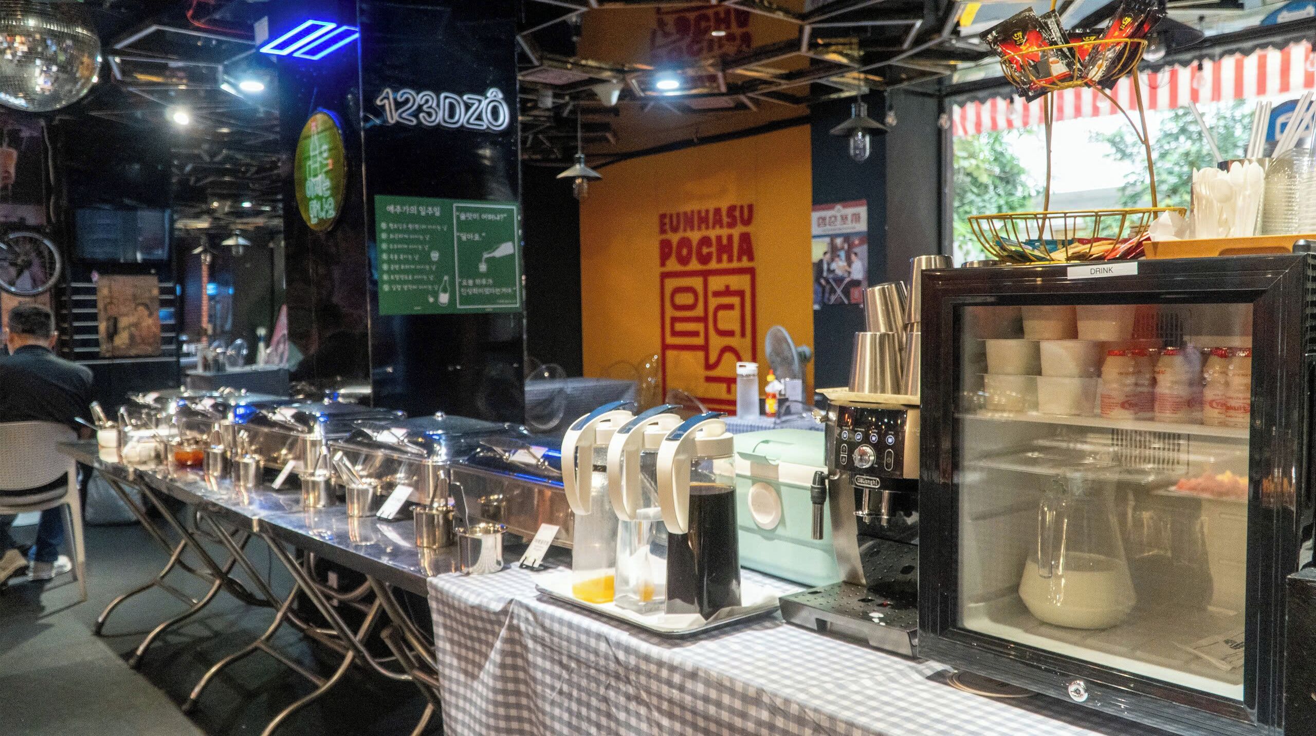 A buffet setup with various food and drink stations, including a coffee machine and a drink dispenser.