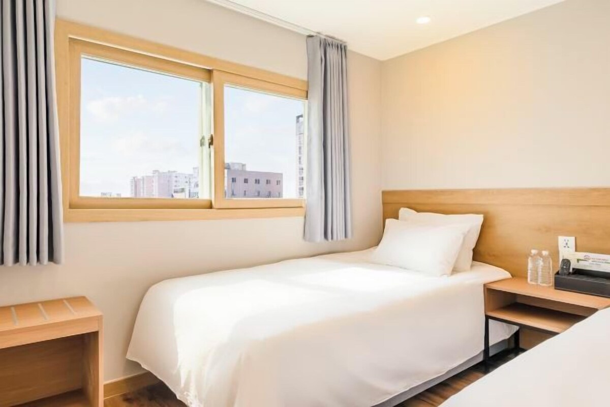 Quarto de hotel com uma cama, mesa de cabeceira, janela com cortinas e vista para edifícios.