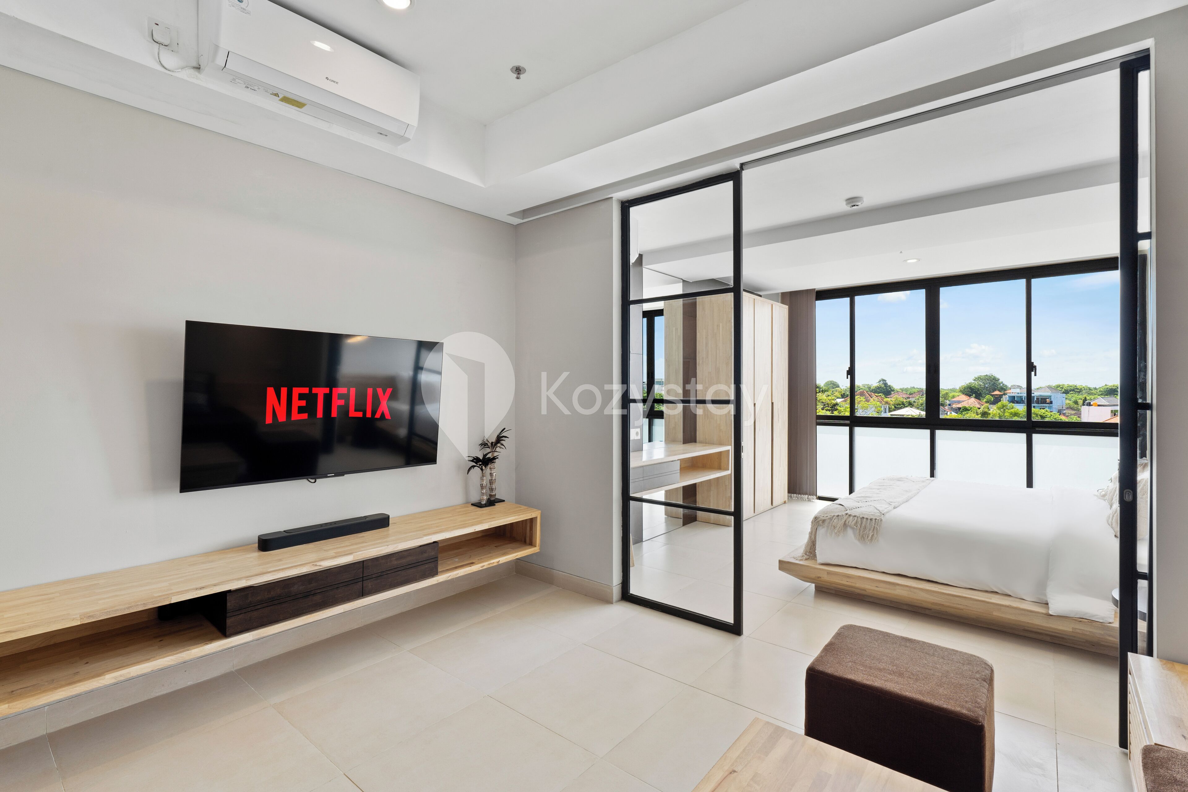 Camera d'hotel moderna con una grande televisione a schermo piatto, un tavolino consolle in legno, un letto con vista sull'esterno e una porta scorrevole in vetro che conduce a un balcone.