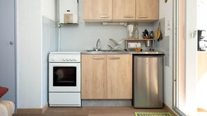 Eine kleine Küche mit Holzausstattung, einem Edelstahlkühlschrank, einem weißen Backofen und einem Spülbecken.
