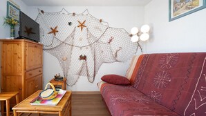 Ein Wohnzimmer mit einem Holzkabinett, einem roten Sofa, einem kleinen Tisch mit bunten Teppich und einer Wanddekoration mit Seesternen und Fischernetzen.