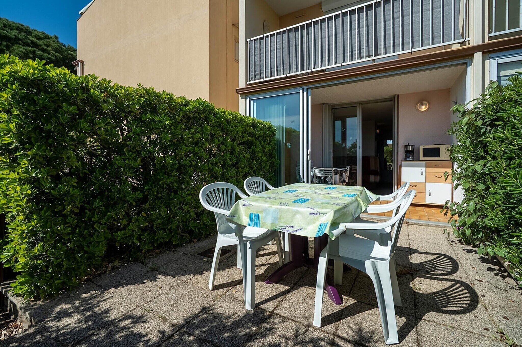 An outdoor patio with a table and chairs, a balcony, and a view of a building.