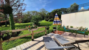 A wooden deck with a metal table and chairs, surrounded by a garden with a wooden fence and potted plants.