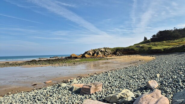 A pebble beach with a rocky outcrop and a view of the sea.