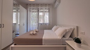 A neatly arranged bedroom with a bed, a bedside table with a plant, and a window with curtains.