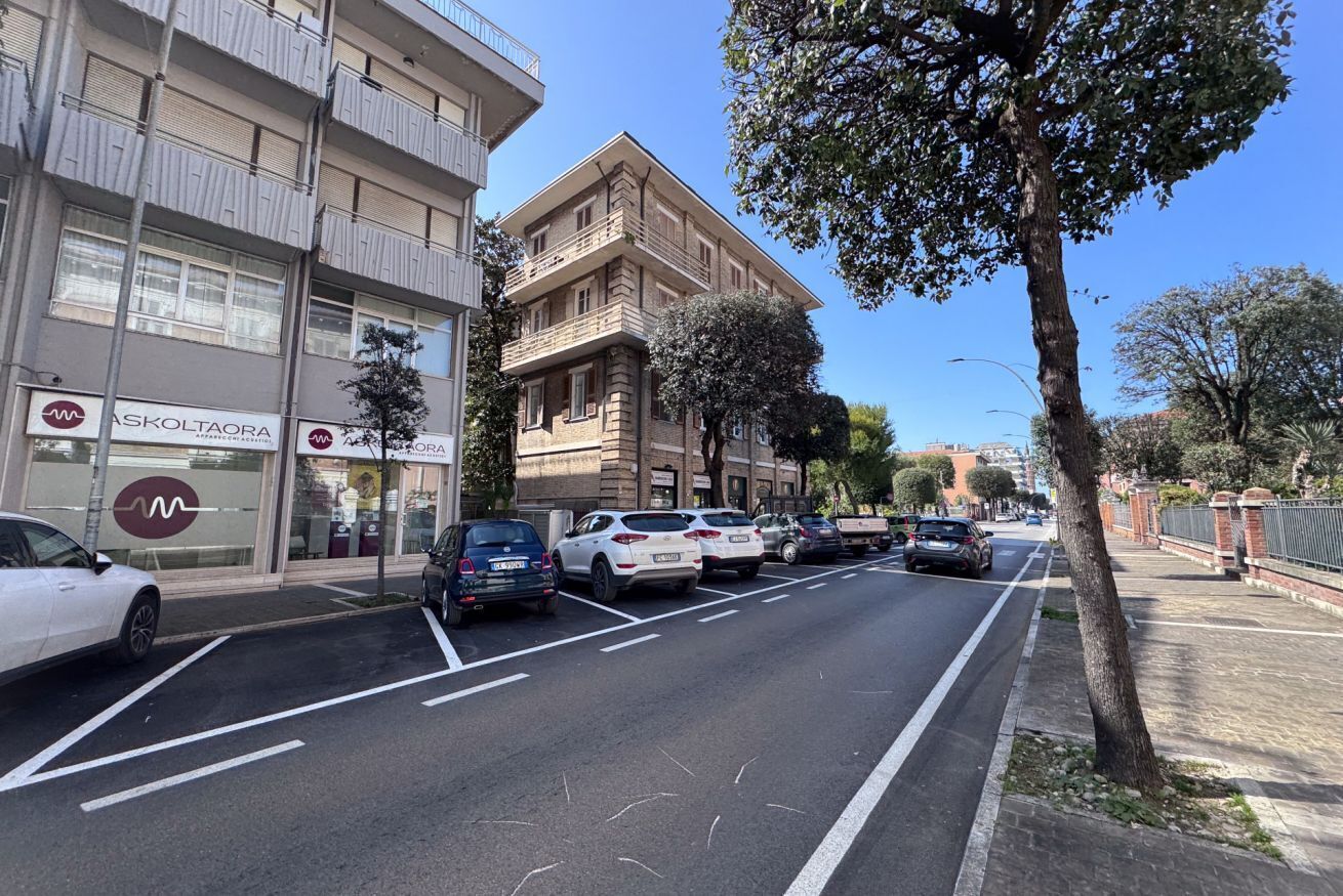 Una calle con coches aparcados, un edificio con el rótulo de un centro médico y una acera arbolada.