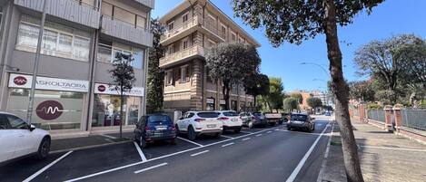 Una calle con coches aparcados, un edificio con el rótulo de un centro médico y una acera arbolada.