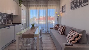 A modern living space with a dining area, sofa, and a view of a building through sheer curtains.