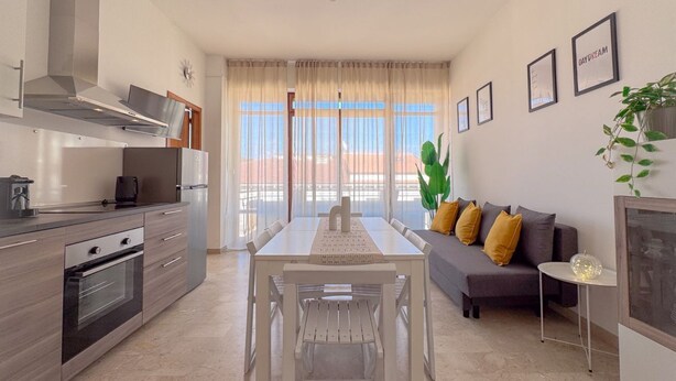 A modern kitchen with a dining table and chairs, a sofa with cushions, and a small side table.