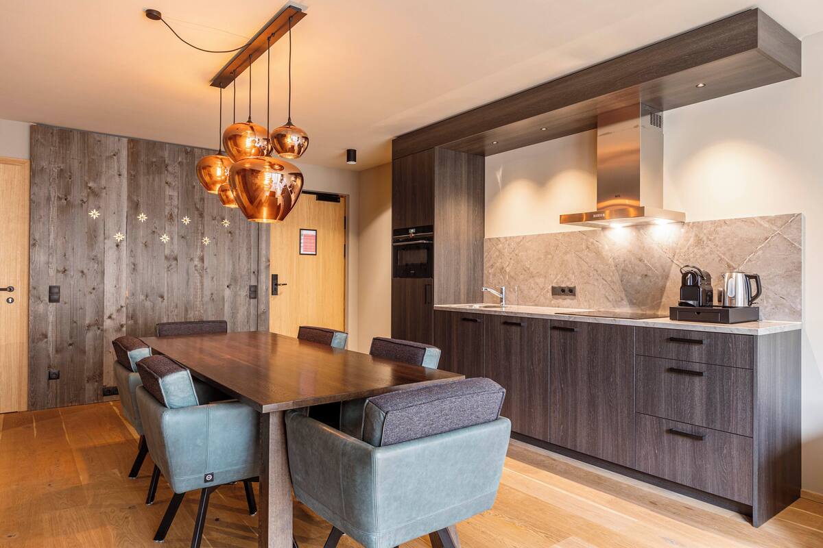 Una cocina moderna con una mesa de comedor de madera, sillas tapizadas en gris y un horno empotrado.