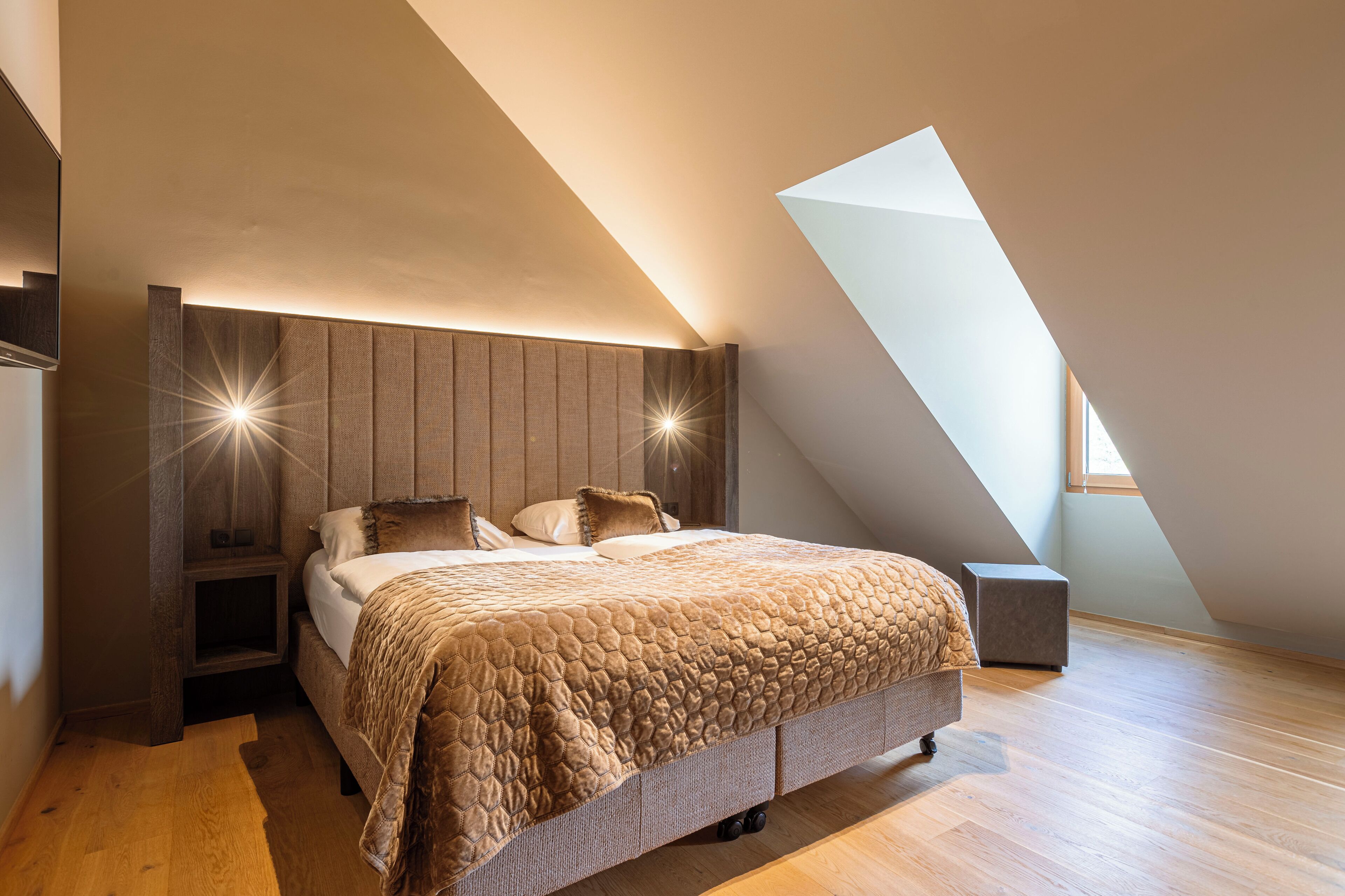 Een slaapkamer met een schuine plafond, een bed met een gewatteerde spreidek en nachtkastjes met een kleine bedlamp.