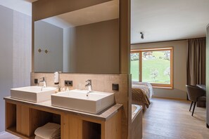 A modern bathroom with two sinks, a large mirror, and a view of a garden through a window. - Montafon Suites Schruns by ALPS RESORTS (Schruns)