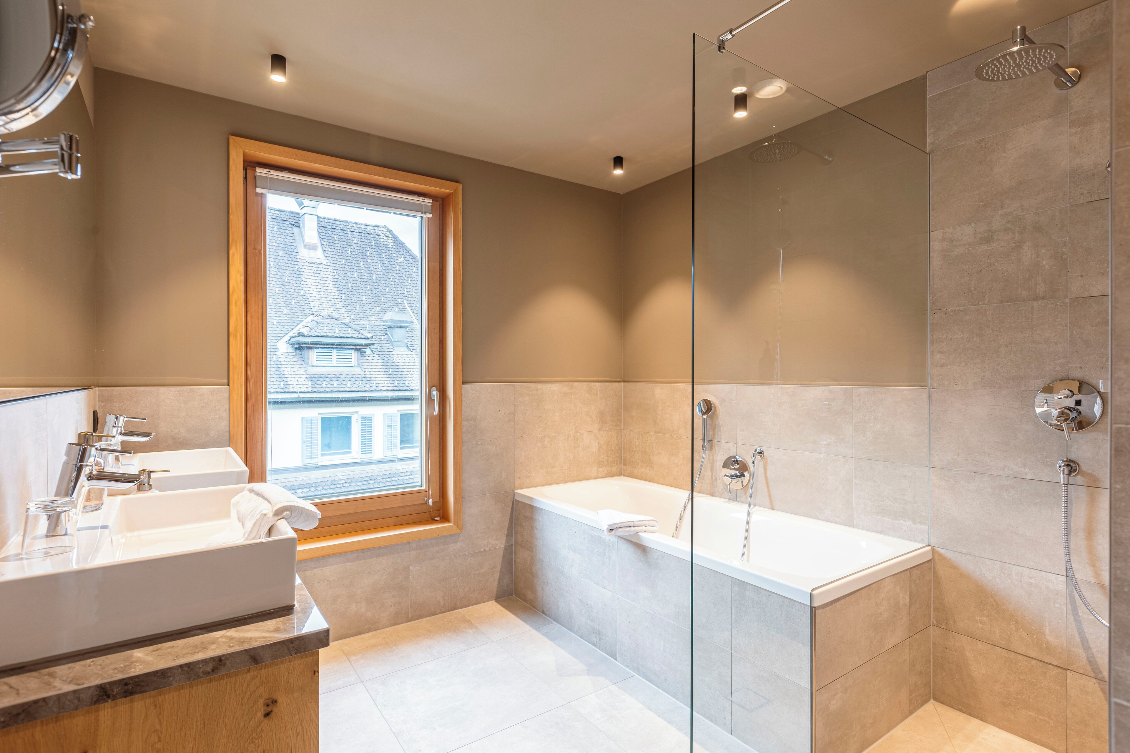 Een moderne badkamer met een badkuip, een douche met glazen wanden en een raam voor natuurlijk licht.