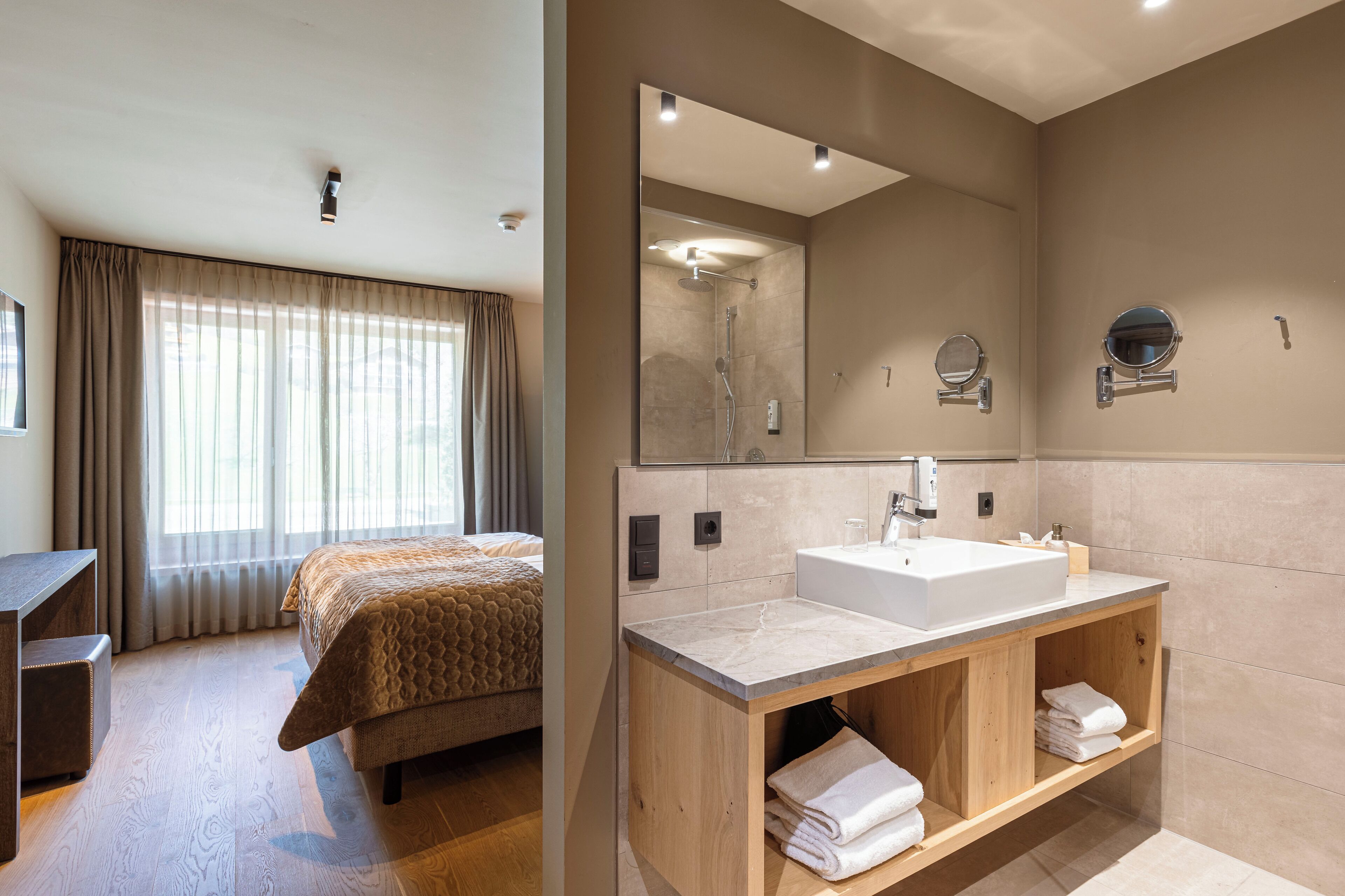 A modern hotel room with a bed, a wooden vanity with a sink, and a large mirror.