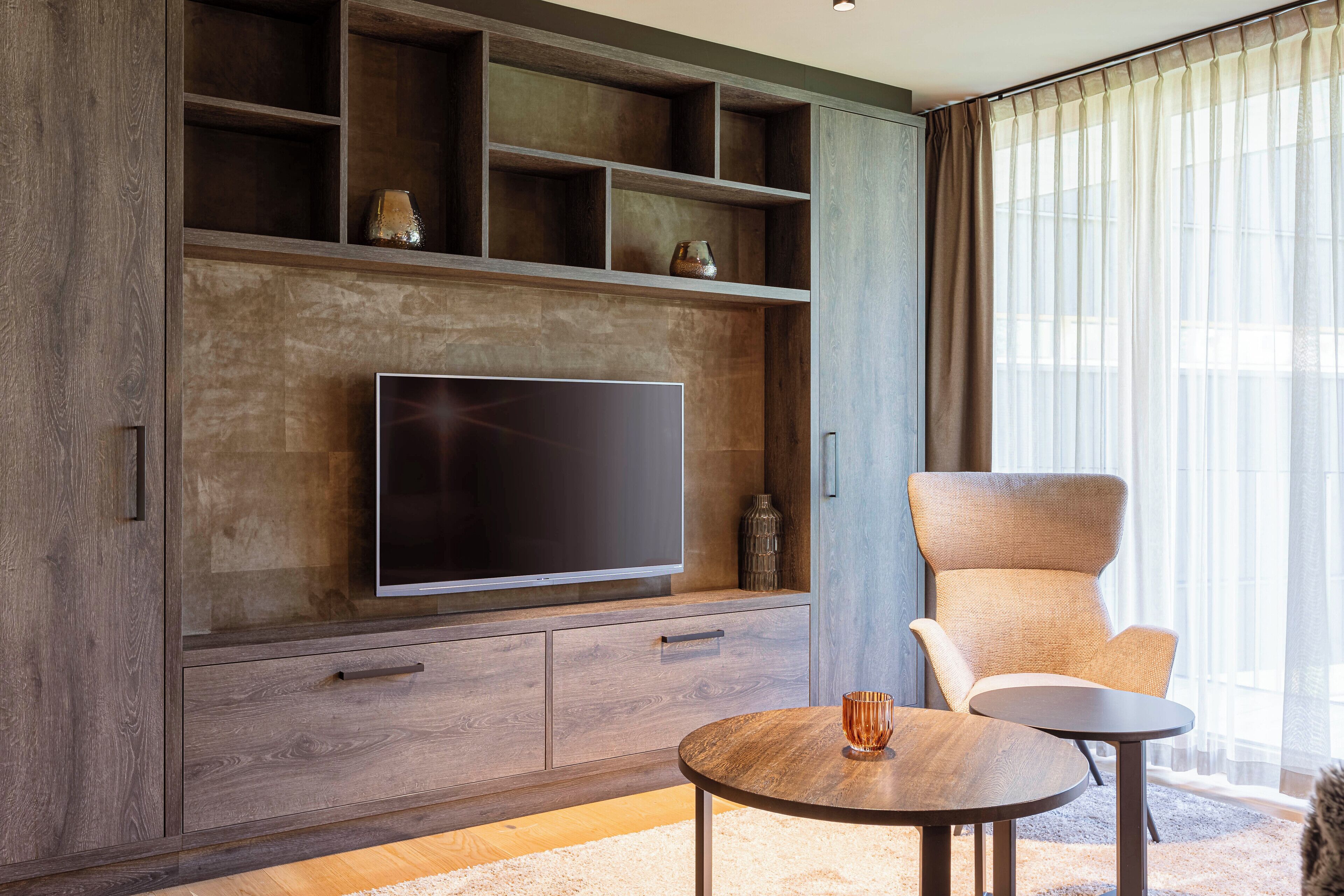 Una sala de estar moderna con un televisor de pantalla plana grande, estanterías de madera, un sillón cómodo y una mesa de centro redonda.