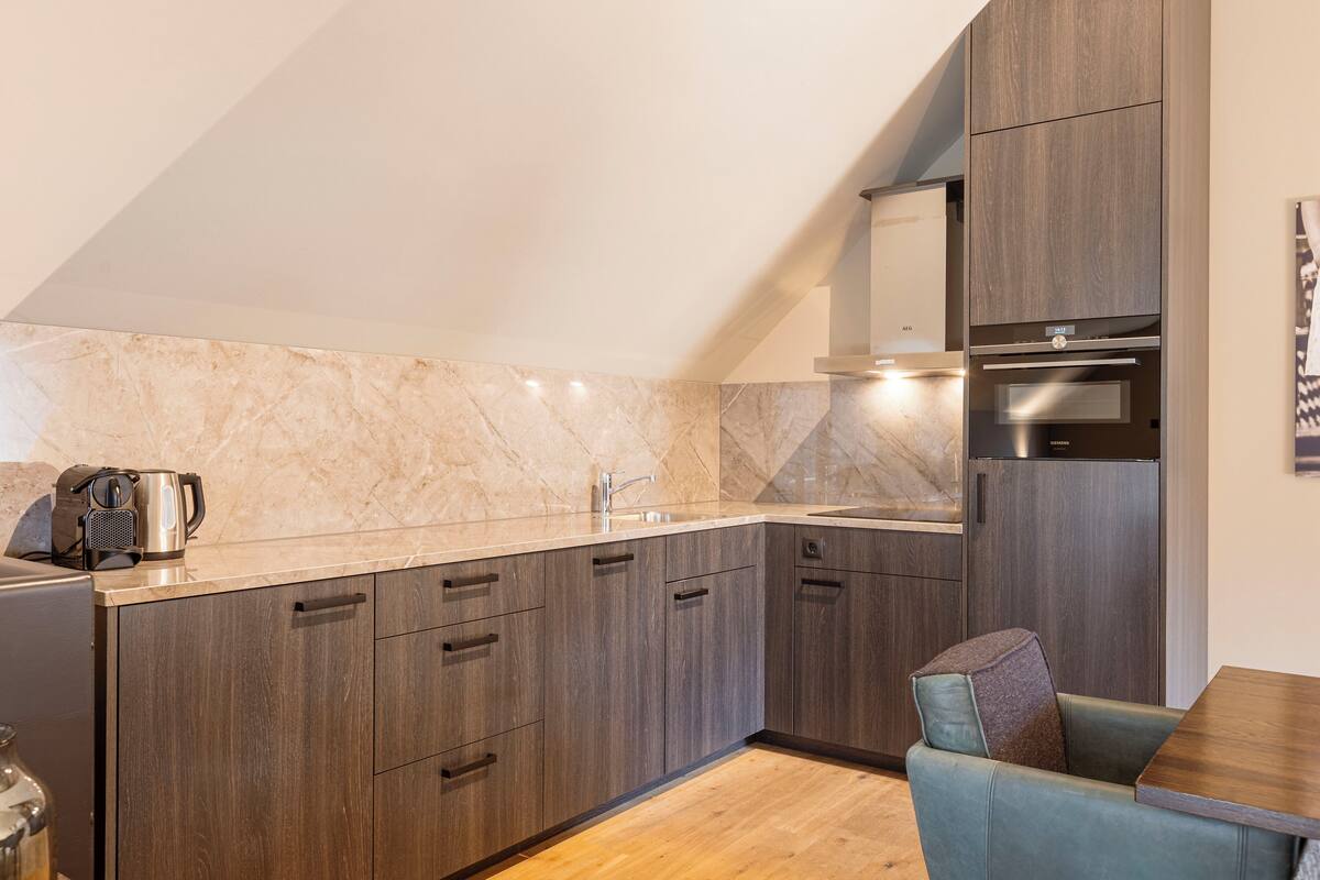 Una cocina moderna con armarios de madera oscura, un salpicadero de mármol y un horno empotrado.