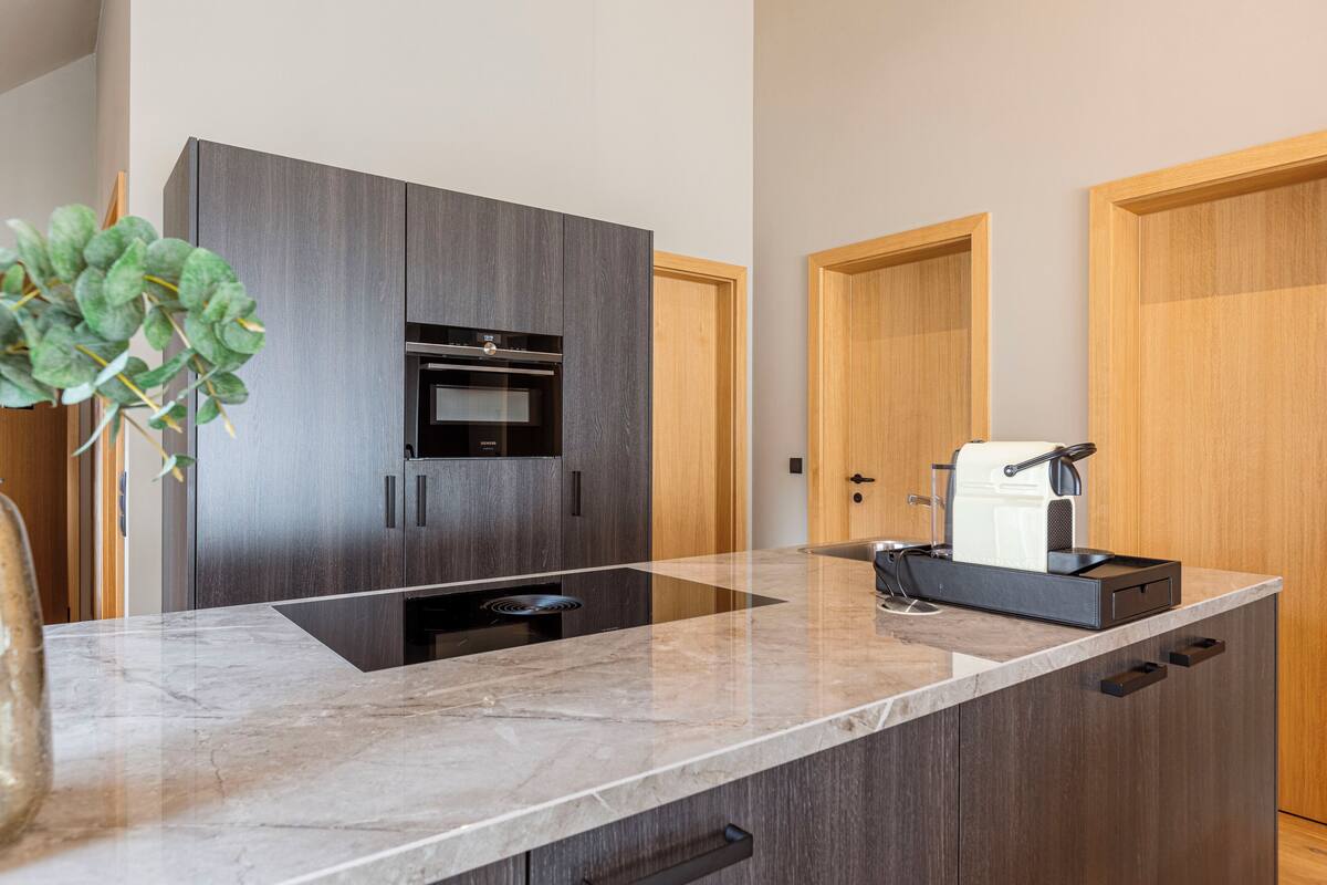 Una cocina moderna con armarios de madera oscura, horno empotrado y cafetera sobre la encimera.