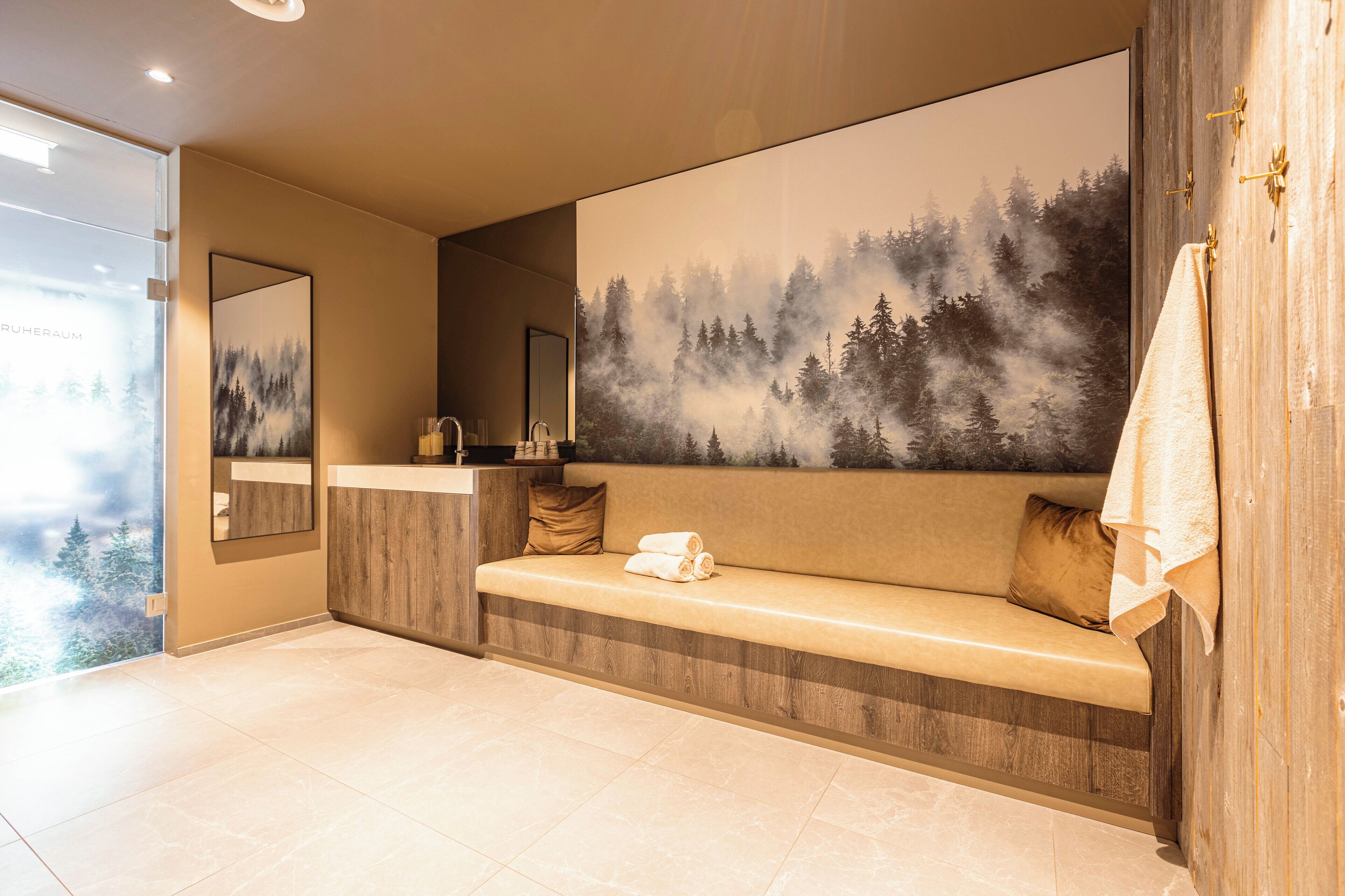 A modern bathroom with a large mirror, a bench with towels, and a wall-mounted sink.