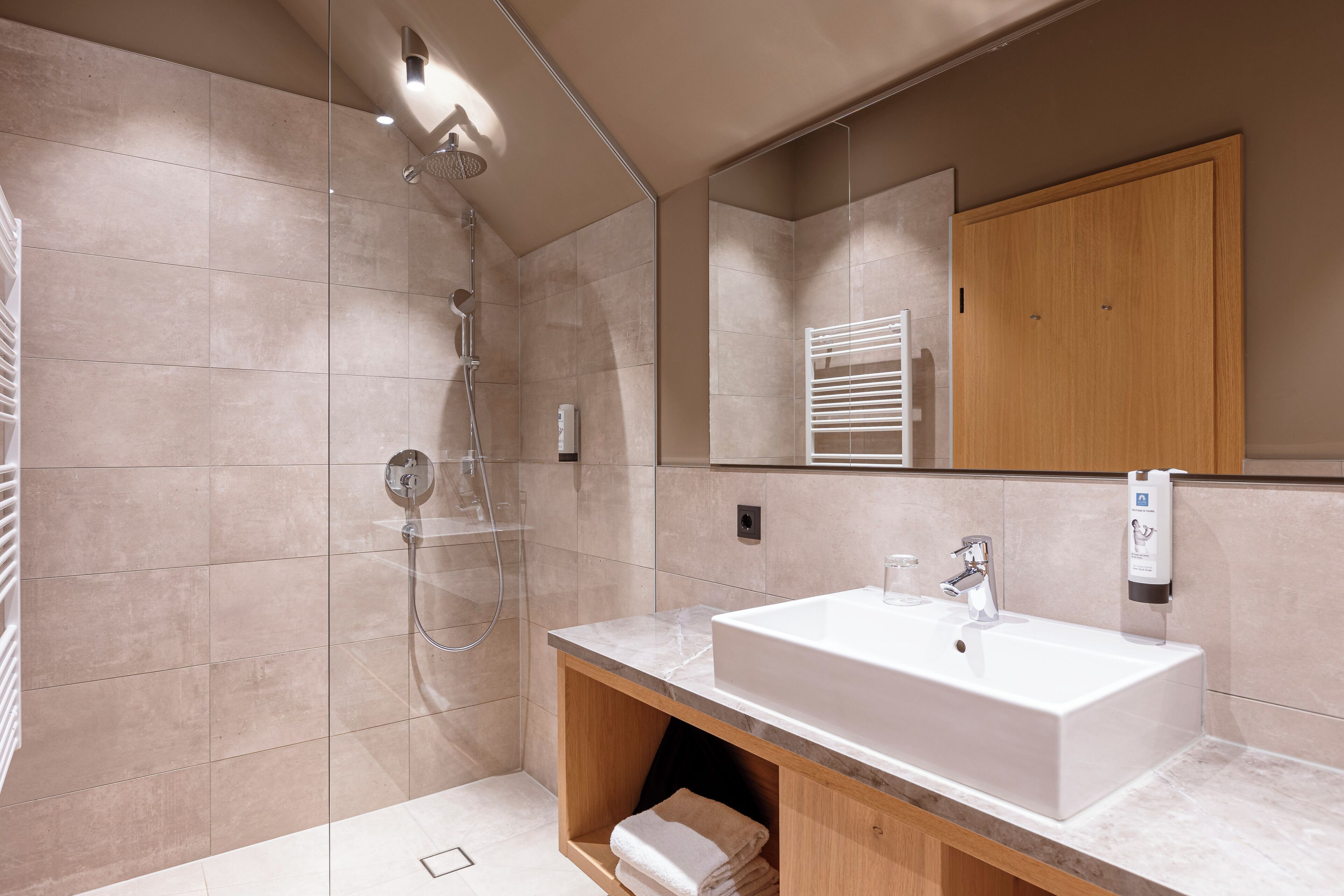 A modern bathroom with a large sink, a shower, and a wooden vanity.