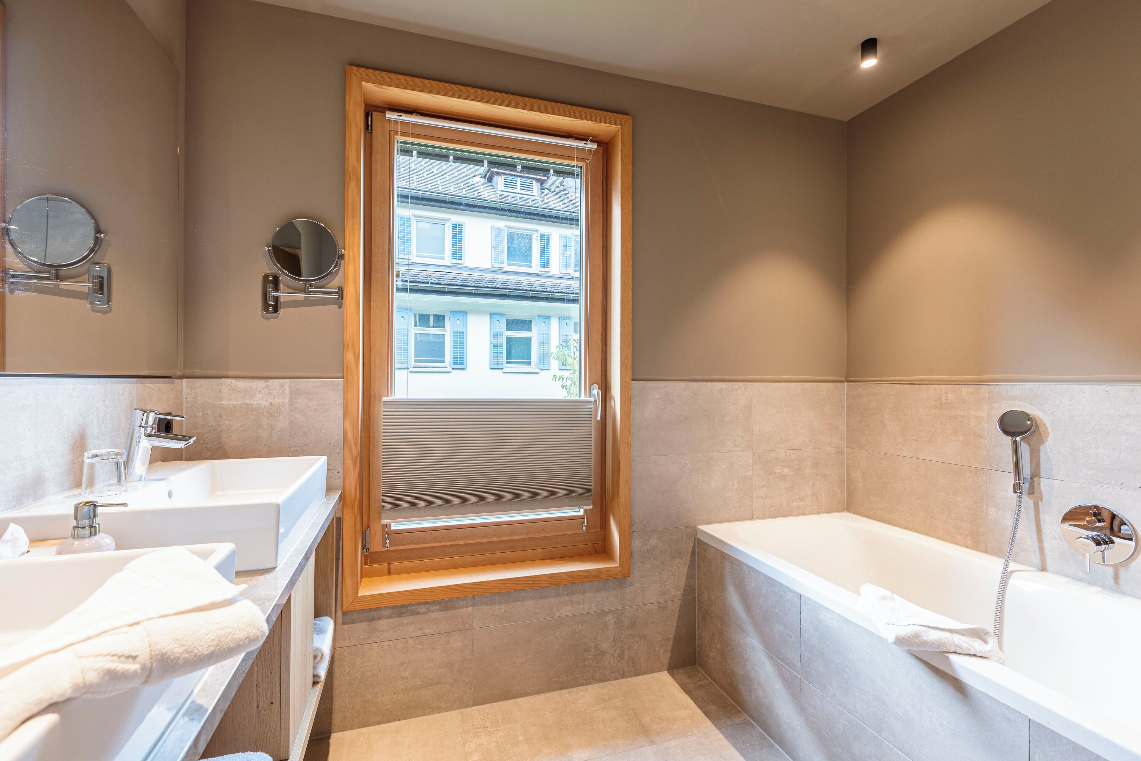 A modern bathroom with two sinks, a bathtub, and a window with blinds.