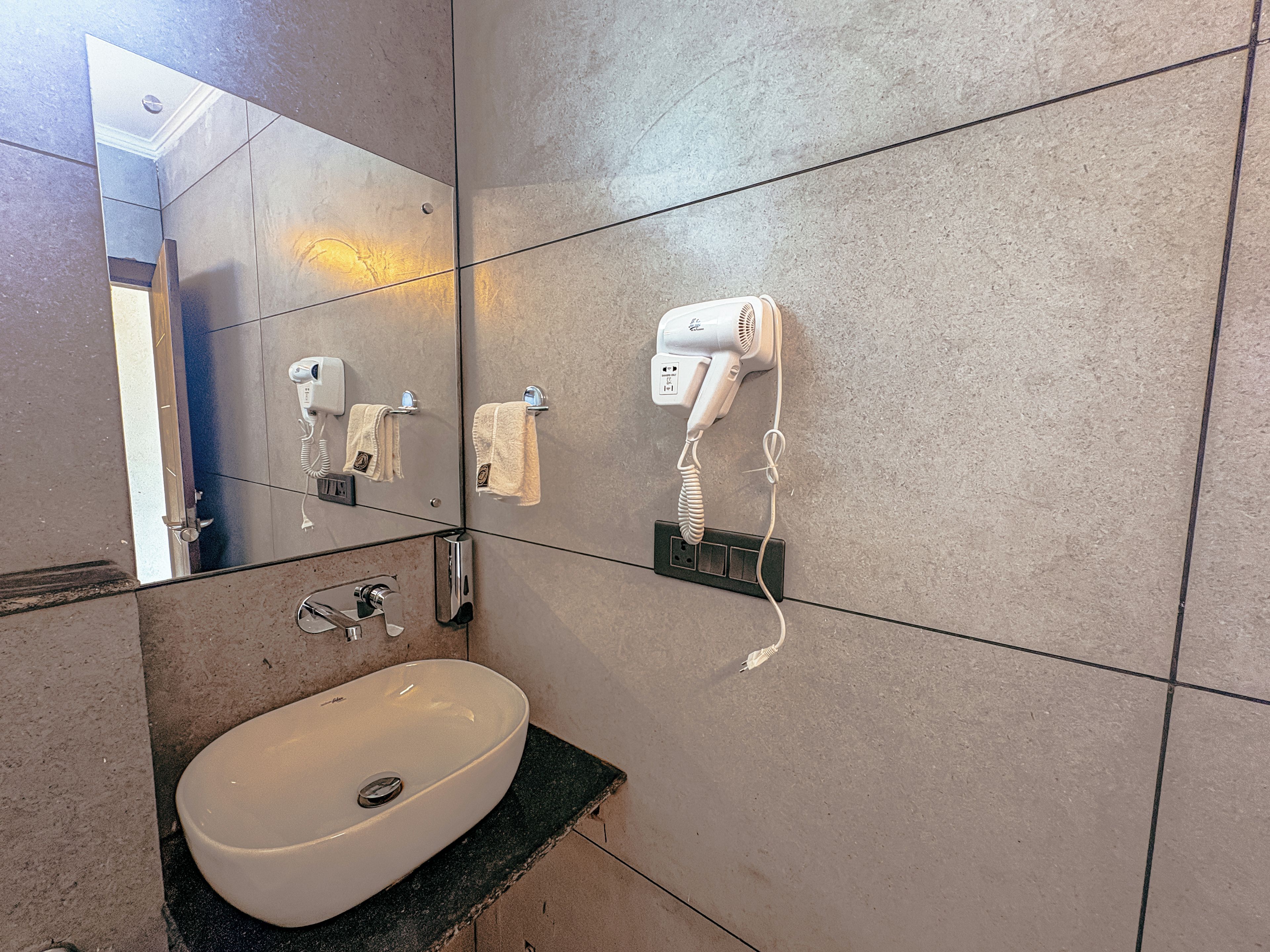 A bathroom with a white sink, a hairdryer, and a mirror reflecting the room.