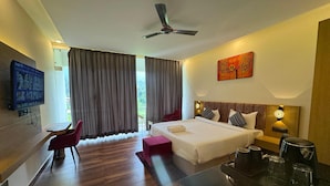 A hotel room with a bed, a desk, a chair, a TV, and a painting. - Nakshville  (Bhimtal)