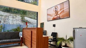 A reception area with a wooden desk, a sofa, a computer, and a Buddha statue. - Nakshville  (Bhimtal)