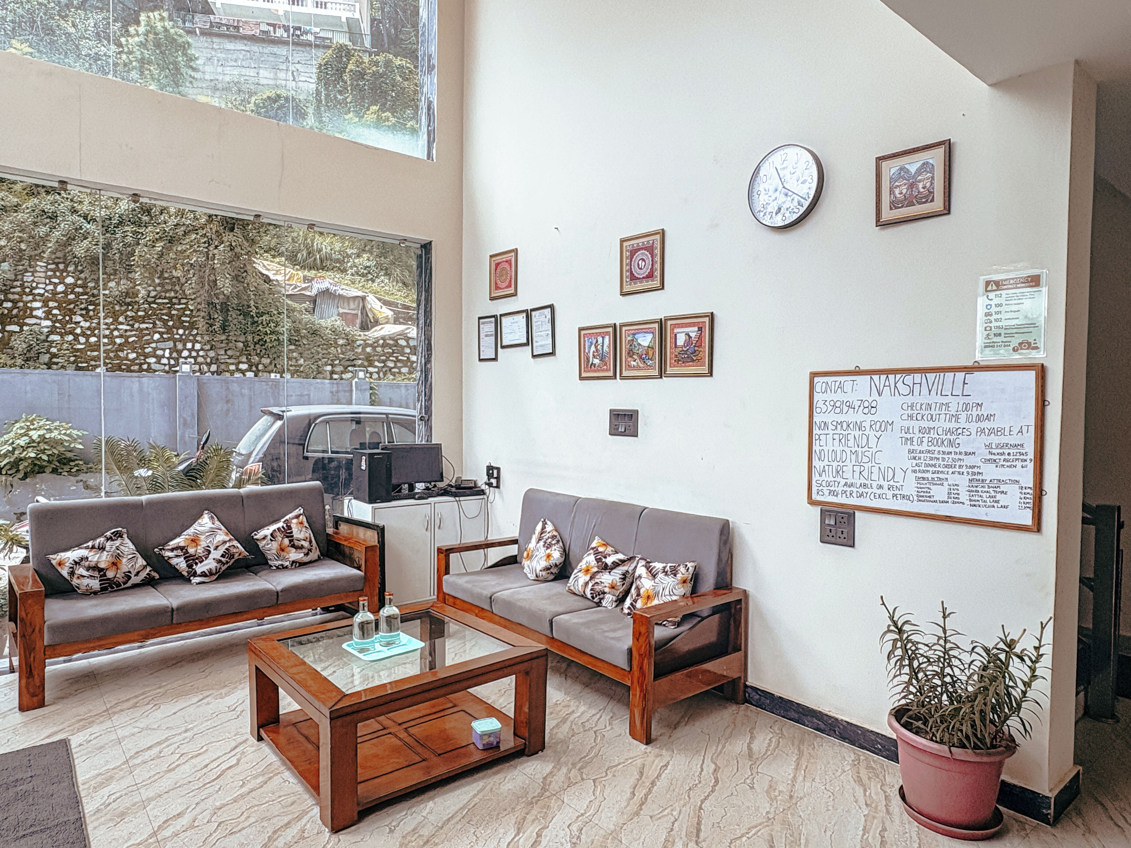 Ein Zimmer mit zwei Sofas, einem Couchtisch, einer Topfpflanze, einem Computer und einer Wand mit gerahmten Bildern und einer Pinnwand.