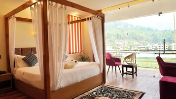 Una cama con dosel y cortinas translúcidas, vista a un paisaje verde y un balcón con sillas de mimbre.