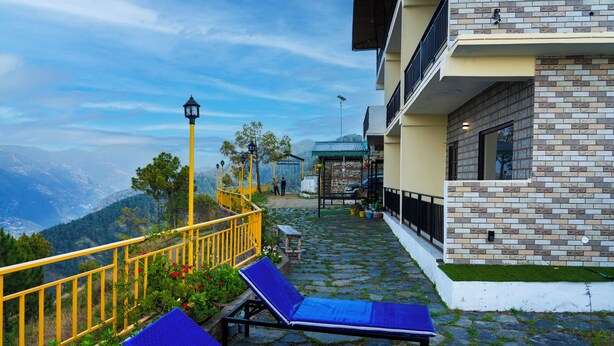 A terrace with blue lounge chairs, a yellow railing, and a stone pathway leading to a building with a brick facade. - Orchard Green Shimla (Shimla)