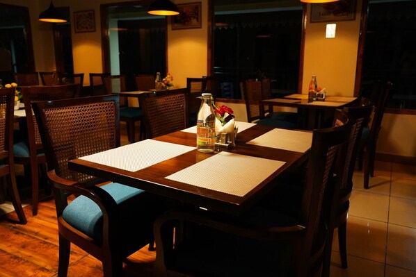 A restaurant with wooden tables and chairs, a bottle of diet tonic water, and a vase with red flowers on the table.