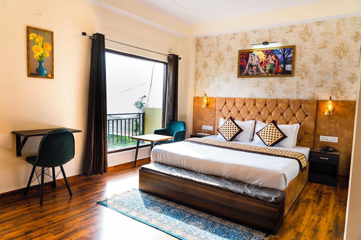 A hotel room with a bed, a desk, a chair, a balcony, and a painting on the wall.